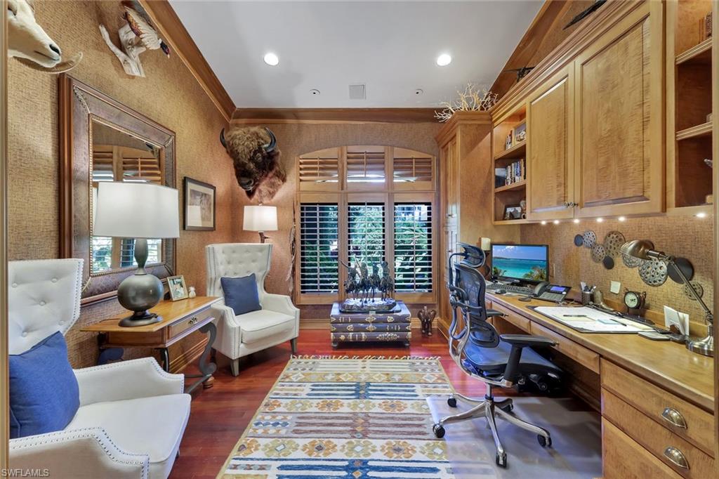 Dedicated office space featuring extensive built-in wooden cabinetry, recessed lighting, wood-finish flooring, and arched windows with plantation shutters