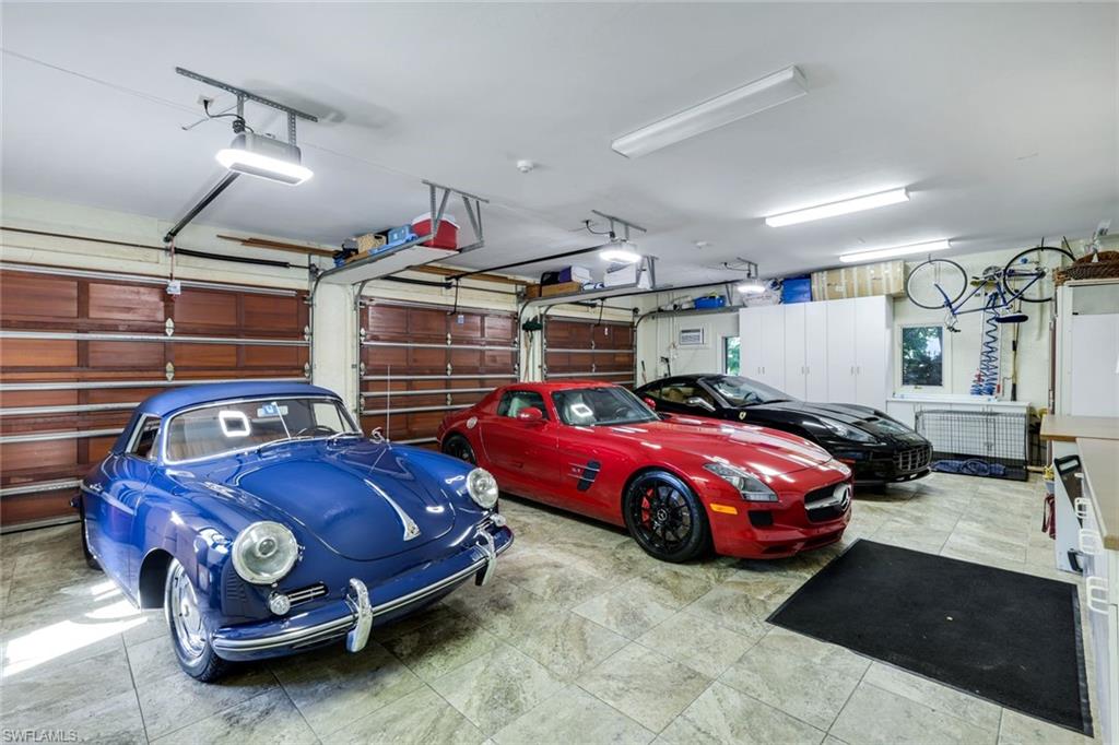 Spacious garage featuring tiled flooring, three paneled garage doors, overhead fluorescent lighting, and built-in white cabinetry