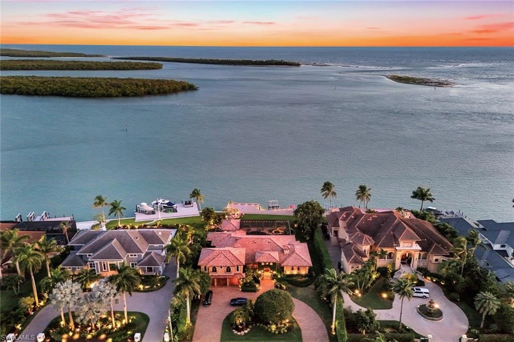 Waterfront property featuring a private boat dock, lush tropical landscaping, and a circular driveway