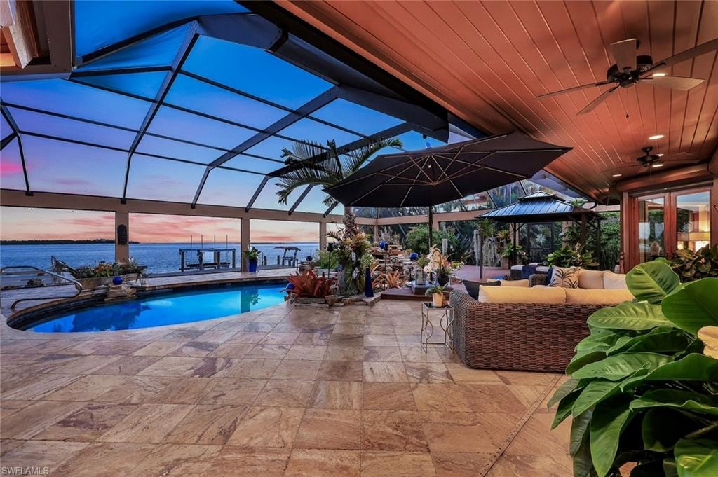 Travertine tile patio featuring a screened enclosure, built-in swimming pool, wood-paneled ceiling, and direct access to the water