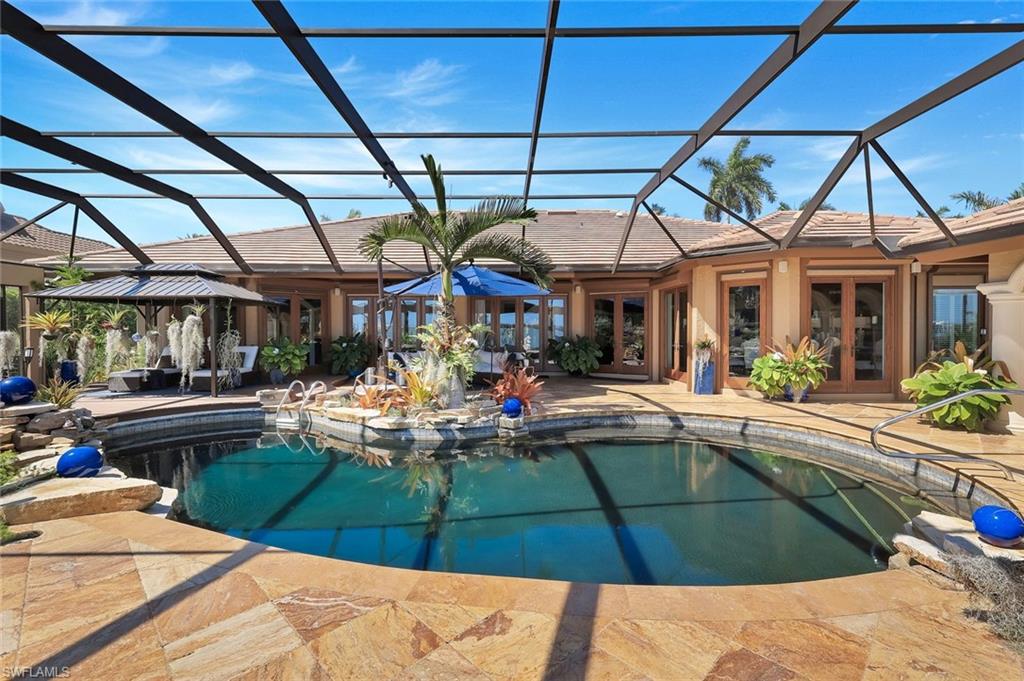 Screen-enclosed pool area featuring a freeform swimming pool, extensive stone paver decking, and a built-in spa with rock accents