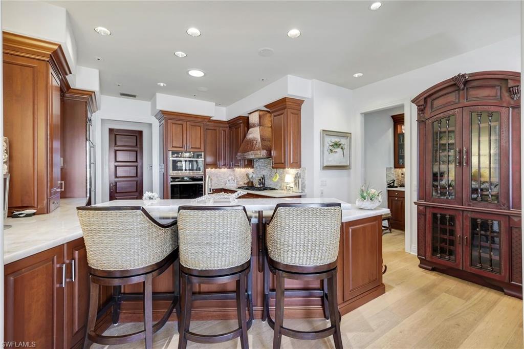 Gourmet kitchen featuring wood cabinetry, stainless steel double ovens, recessed lighting, a built-in wine cabinet, and wood-finish flooring