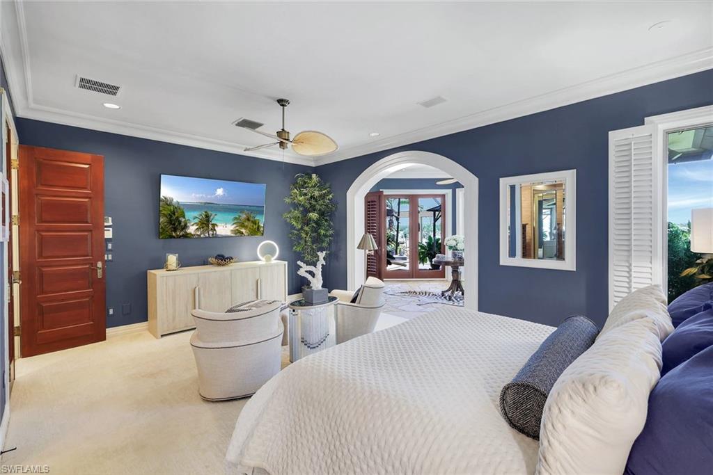 Bedroom featuring a broad arched doorway, rich wood-panel door, white crown molding, a ceiling fan, and window shutters