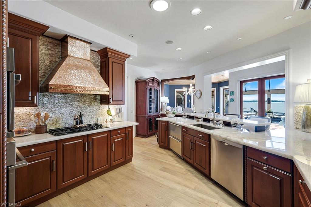 Gourmet kitchen featuring rich wood cabinetry, light-toned wood-finish flooring, a hammered copper range hood, stainless steel appliances, and solid surface countertops