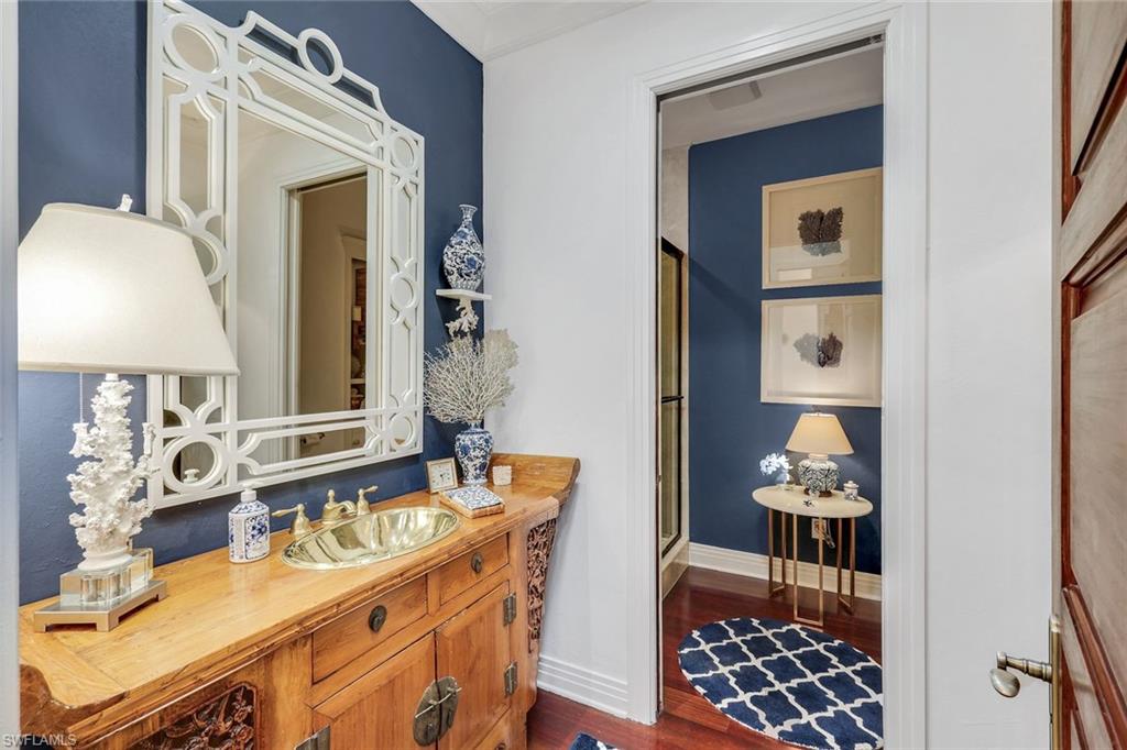 Vanity area featuring a brass vessel sink set in a carved wood cabinet, a decorative white mirror, and a deep blue accent wall
