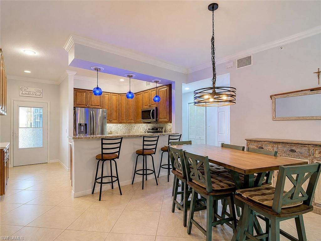 Open-concept dining and kitchen area featuring tile flooring, a breakfast bar with granite countertop, stainless steel appliances, recessed lighting, and a contemporary chandelier