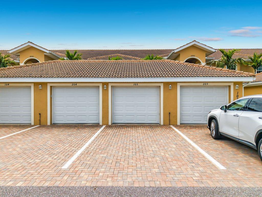 Exterior building featuring stucco finish, tile roof, multiple garage doors, exterior lighting fixtures, and paver driveway