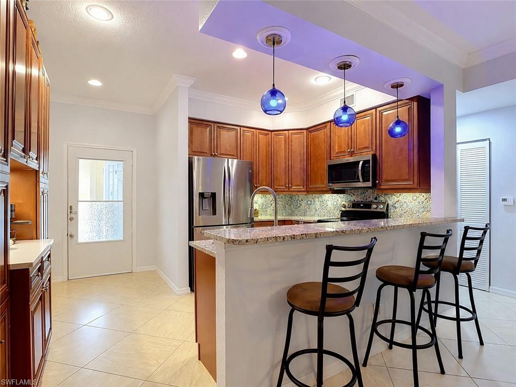 Kitchen featuring wood-finish cabinetry, stainless steel appliances, a breakfast bar with granite countertop, and tile flooring