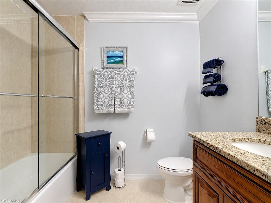 Bathroom featuring a built-in tub with sliding glass doors, tan tiled surround, and crown molding