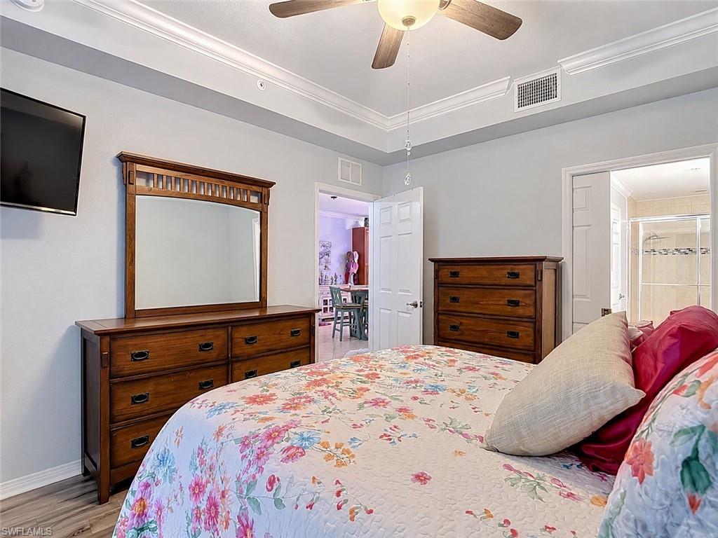 Interior room featuring crown molding, a ceiling fan with integrated lighting, wood-finish flooring, and a doorway leading to The Primary Bathroom and Walk In Closet
