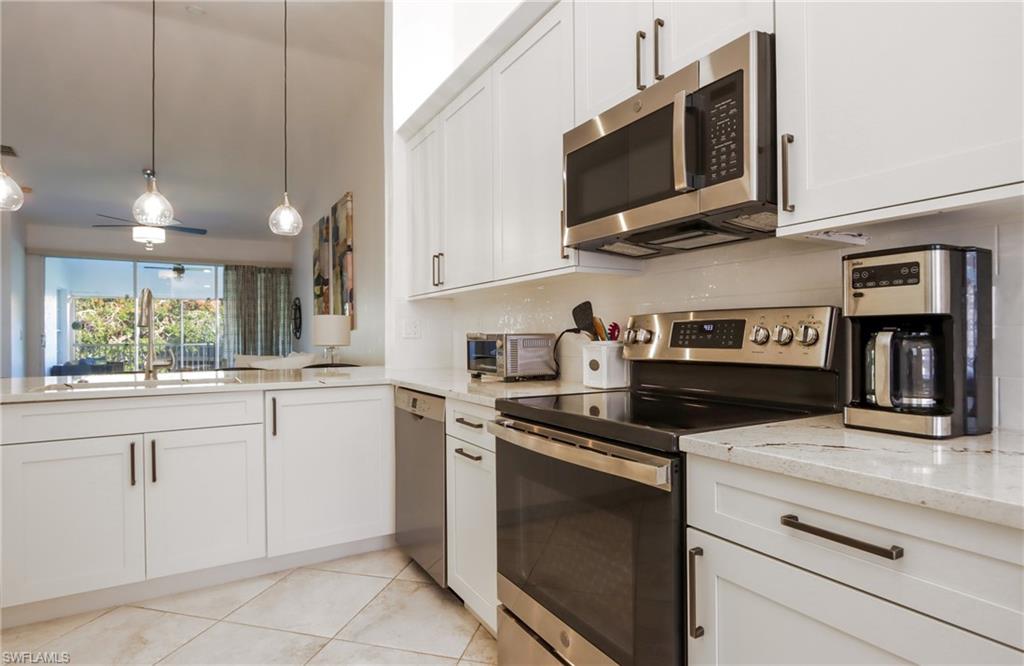Kitchen with appliances with stainless steel finishes, light stone counters, white cabinets, light tile patterned floors, and decorative light fixtures