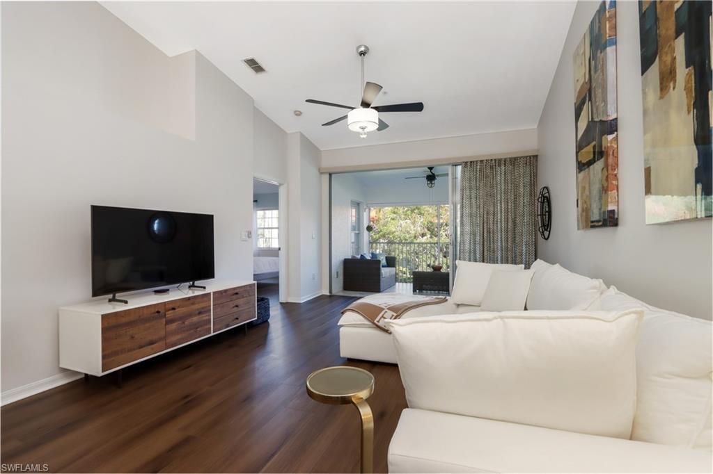 Living room featuring a ceiling fan, dark wood-style flooring, and vaulted ceiling