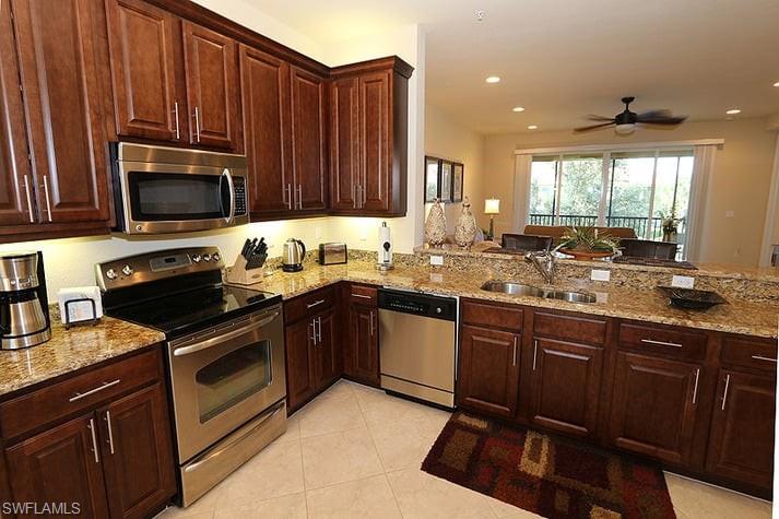 Kitchen featuring stainless steel appliances, kitchen peninsula, light tile patterned floors, light stone countertops, and ceiling fan
