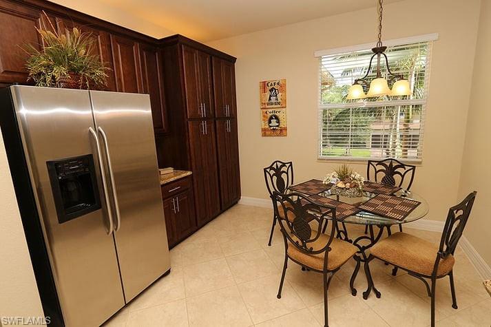 Kitchen featuring stainless steel fridge with ice dispenser, a notable chandelier, light tile patterned floors, pendant lighting, and dark brown cabinetry