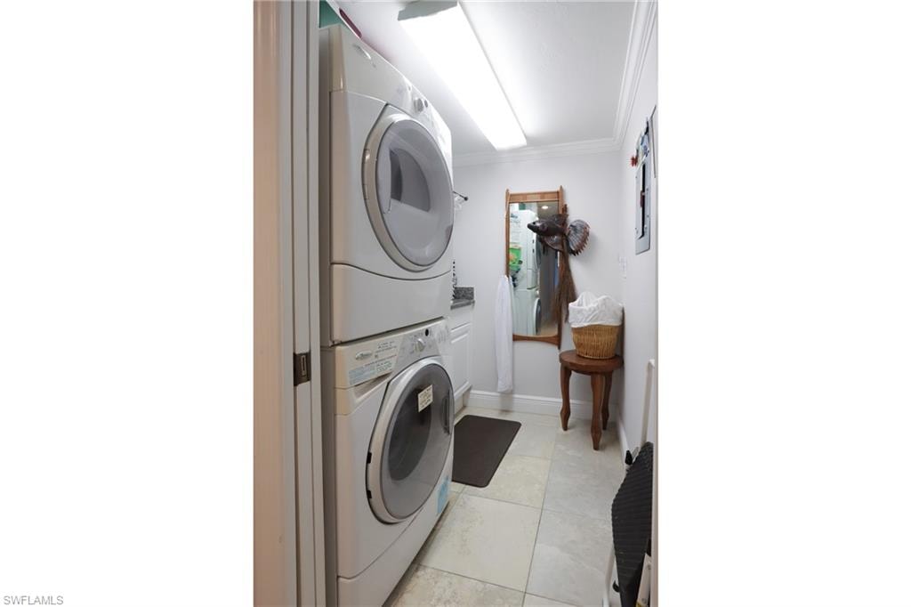 Laundry room featuring stacked washer and clothes dryer, crown molding, and light tile patterned floors