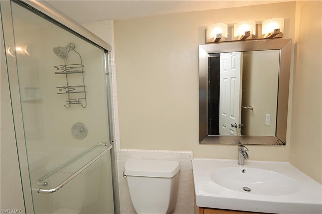 Bathroom featuring vanity, toilet, a shower with door, and tile walls