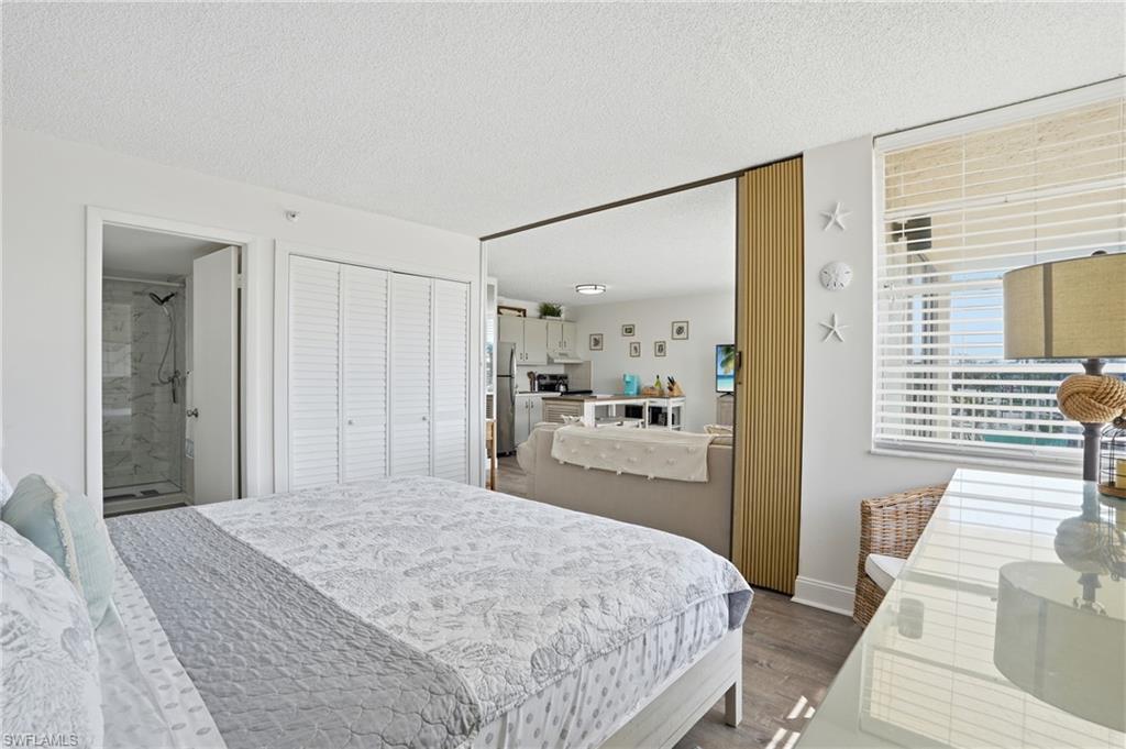 Bedroom area featuring wood-finish flooring, louvered bi-fold closet doors, and a window with horizontal blinds - Virtually Edited Image