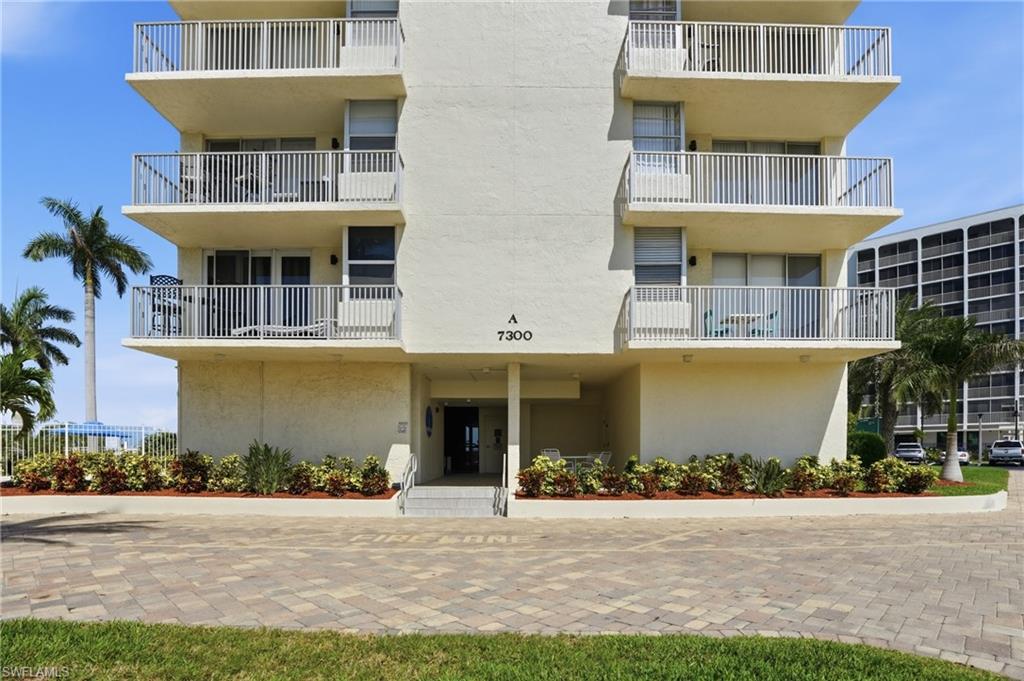 Multi-story residential building featuring private balconies with white railings, a paver driveway, and ground-level landscaping - Virtually Edited Image