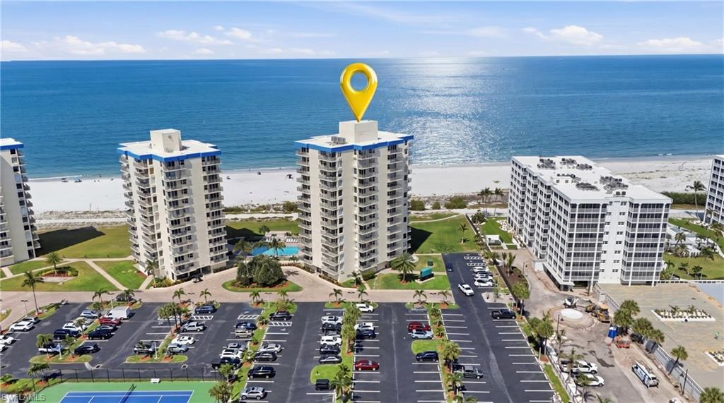 Beachfront high-rise condominium featuring multiple balconies, a swimming pool, tennis court, and ample surface parking - Virtually Edited Image