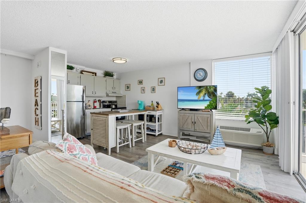 Open-concept living area featuring wood-finish flooring, a kitchen with light-toned cabinetry, stainless steel appliances, and a peninsula with seating - Virtually Edited Image