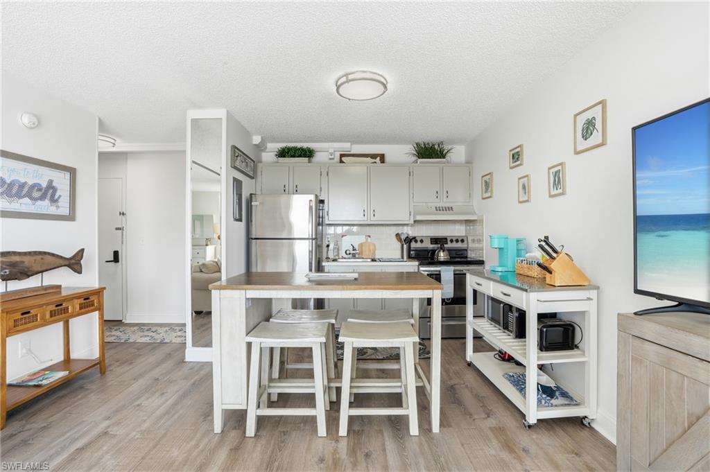 Open-concept kitchen and living area featuring wood-finish flooring, recessed lighting, and a neutral color palette - Virtually Edited Image
