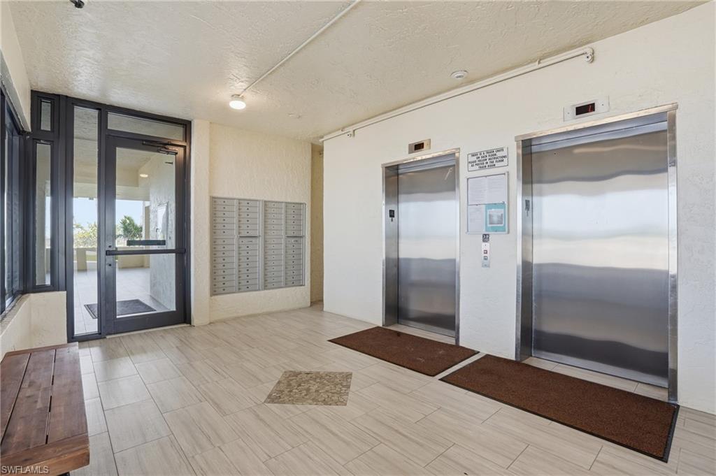 Common area featuring two stainless steel elevators, a wall of individual mailboxes, and wood-finish flooring with an accent tile inlay - Virtually Edited Image