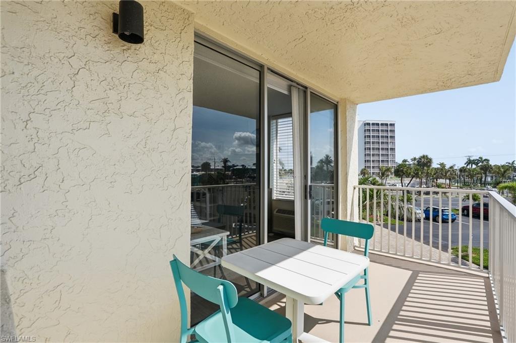 Private balcony featuring textured stucco walls, sliding glass doors with vertical blinds, a white metal railing, and a partial cityscape with palm trees - Virtually Edited Image