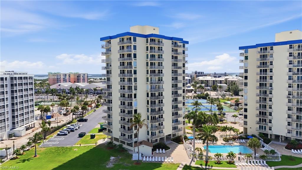 High-rise condominium building featuring multiple private balconies, a ground-level swimming pool, and tennis courts - Virtually Edited Image