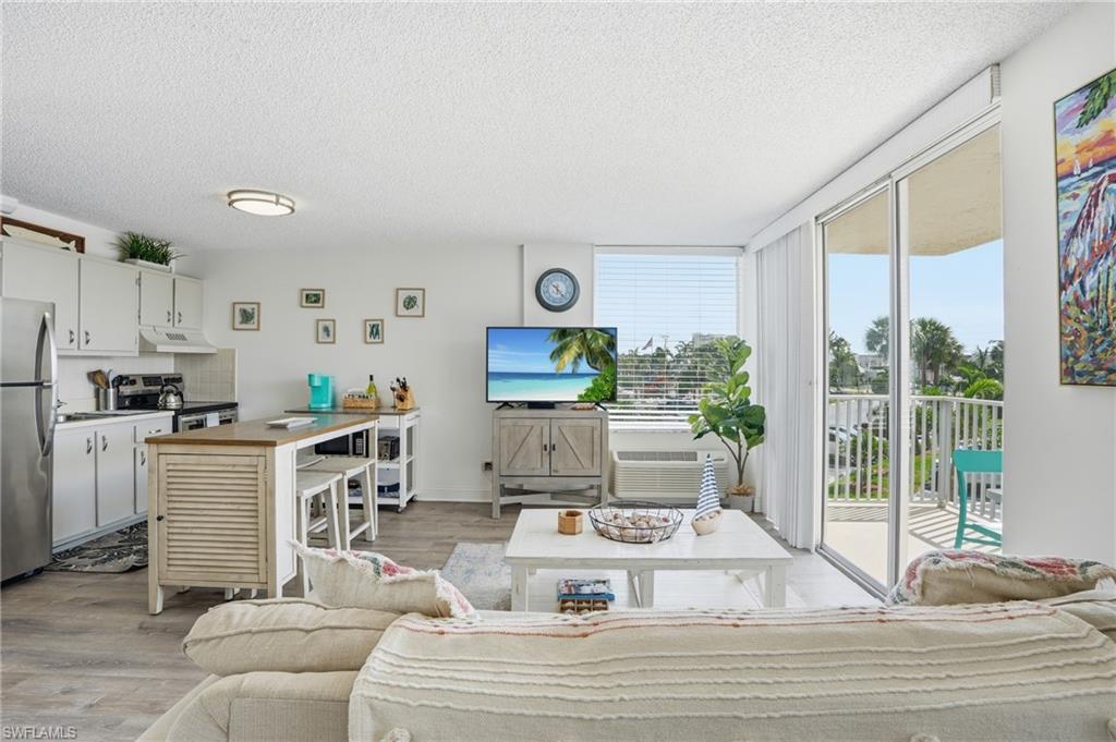 Open concept living area featuring wood-finish flooring, a full kitchen with stainless steel appliances, and a breakfast bar island - Virtually Edited Image