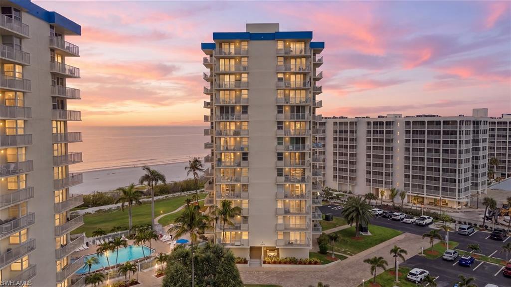 High-rise condominium building featuring multiple private balconies, a ground-level swimming pool, and tropical landscaping - Virtually Edited Image