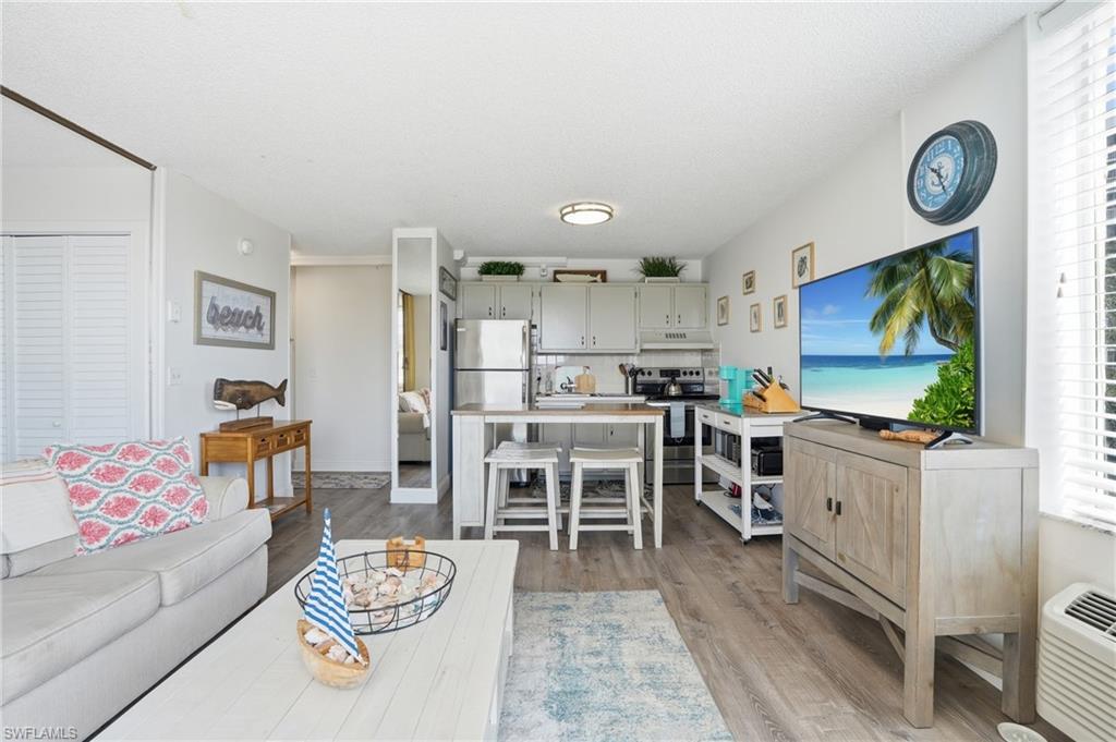 Open-concept living space featuring wood-finish flooring, a kitchen with light-colored cabinetry and stainless steel appliances, and a breakfast bar - Virtually Edited Image