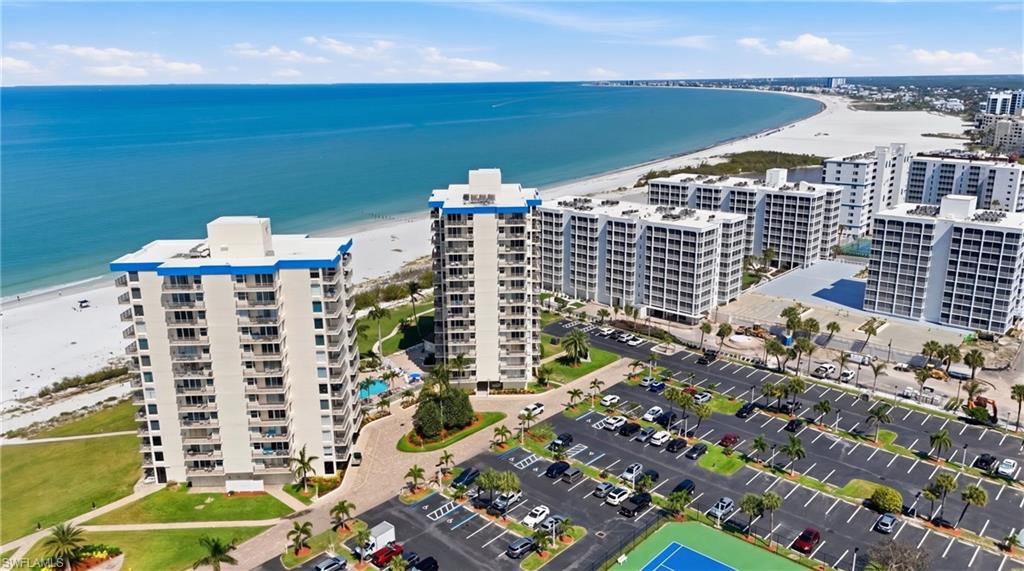 Beachfront high-rise condominiums featuring private balconies, expansive parking facilities, a tennis court, and an outdoor swimming pool area - Virtually Edited Image