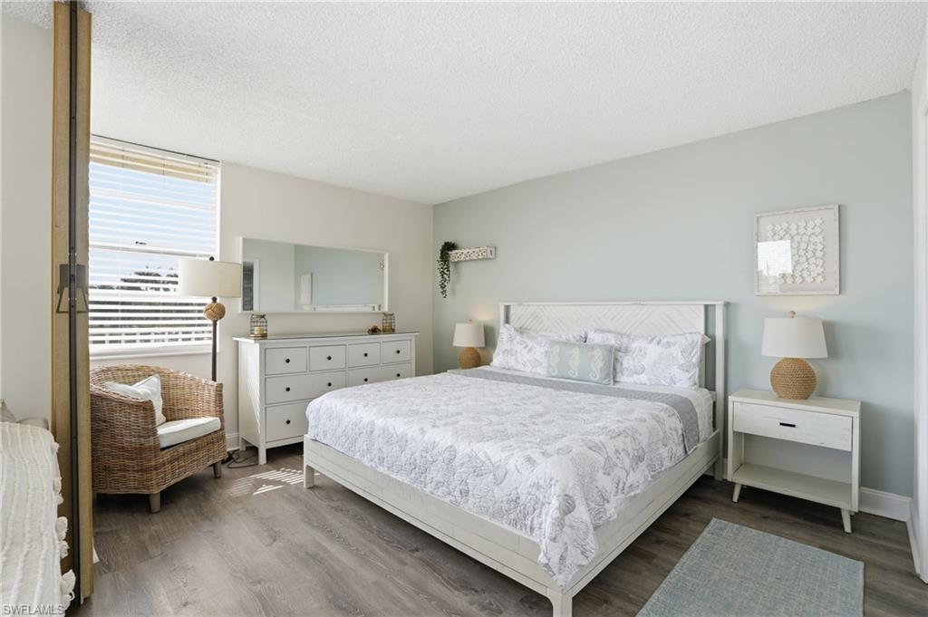Spacious room featuring wood-finish flooring, a large window with horizontal blinds, a white paneled ceiling, and light-colored walls - Virtually Edited Image