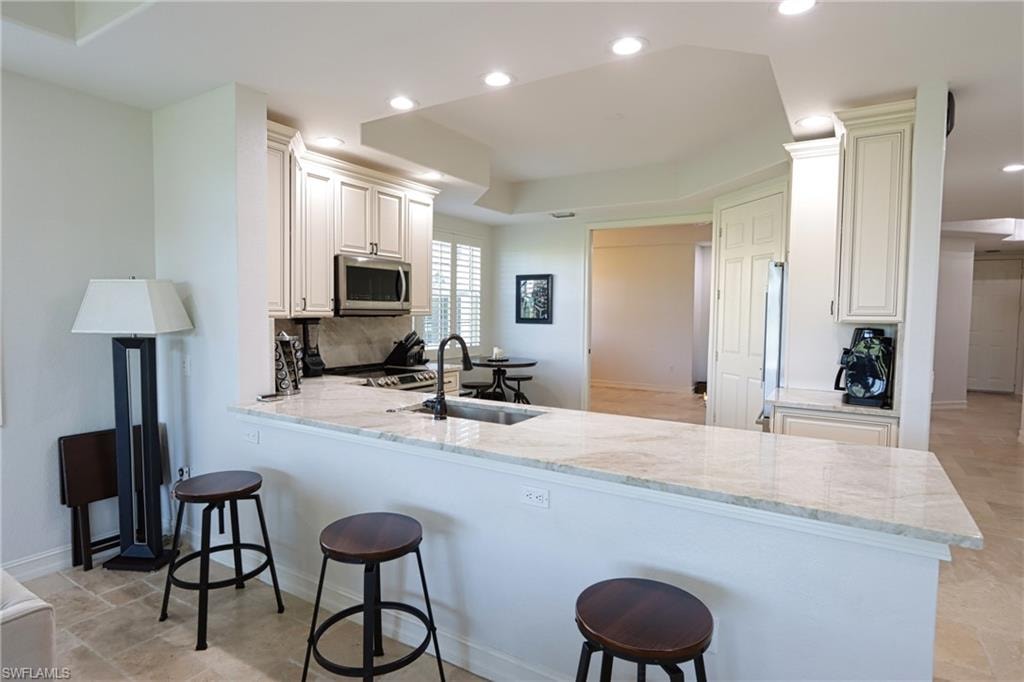 Kitchen featuring tasteful backsplash, sink, a kitchen bar, light stone counters, and kitchen peninsula