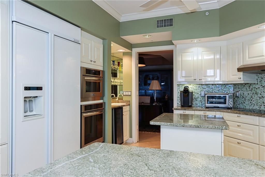 Kitchen with tasteful backsplash, paneled refrigerator, black electric cooktop, ornamental molding, and white cabinets