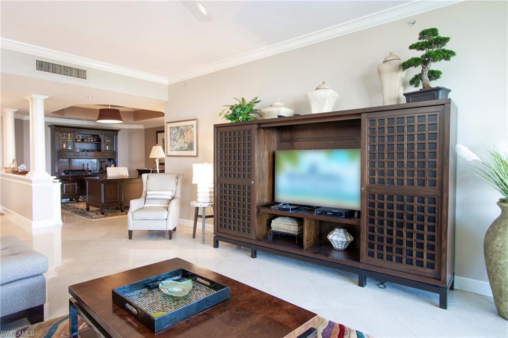 Living room with crown molding, light tile patterned floors, and decorative columns