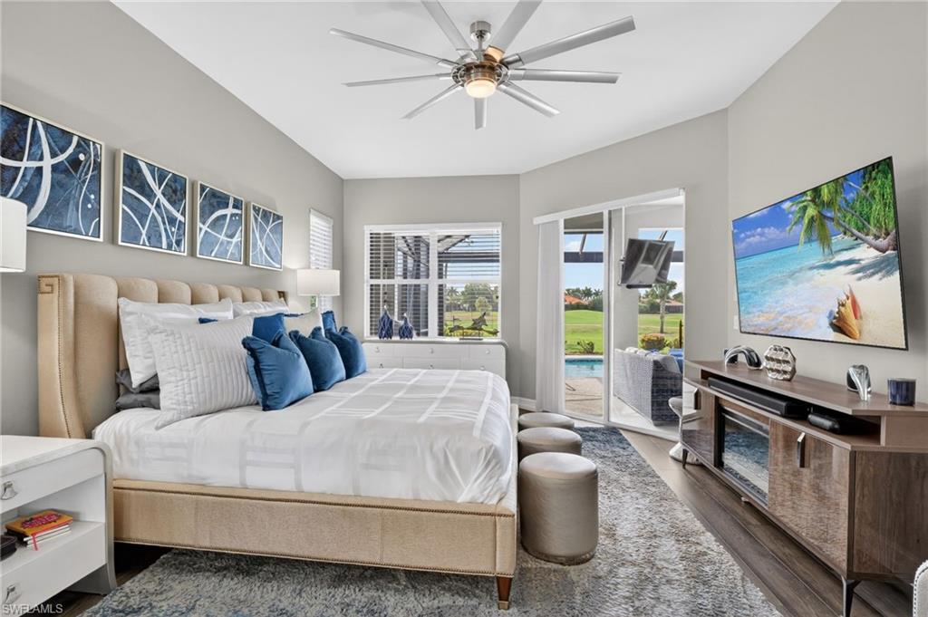 Stunning Primary Suite featuring a ceiling fan with light, wood-finish flooring, and a large sliding glass door opening to an outdoor lanai with a pool and golf course beyond