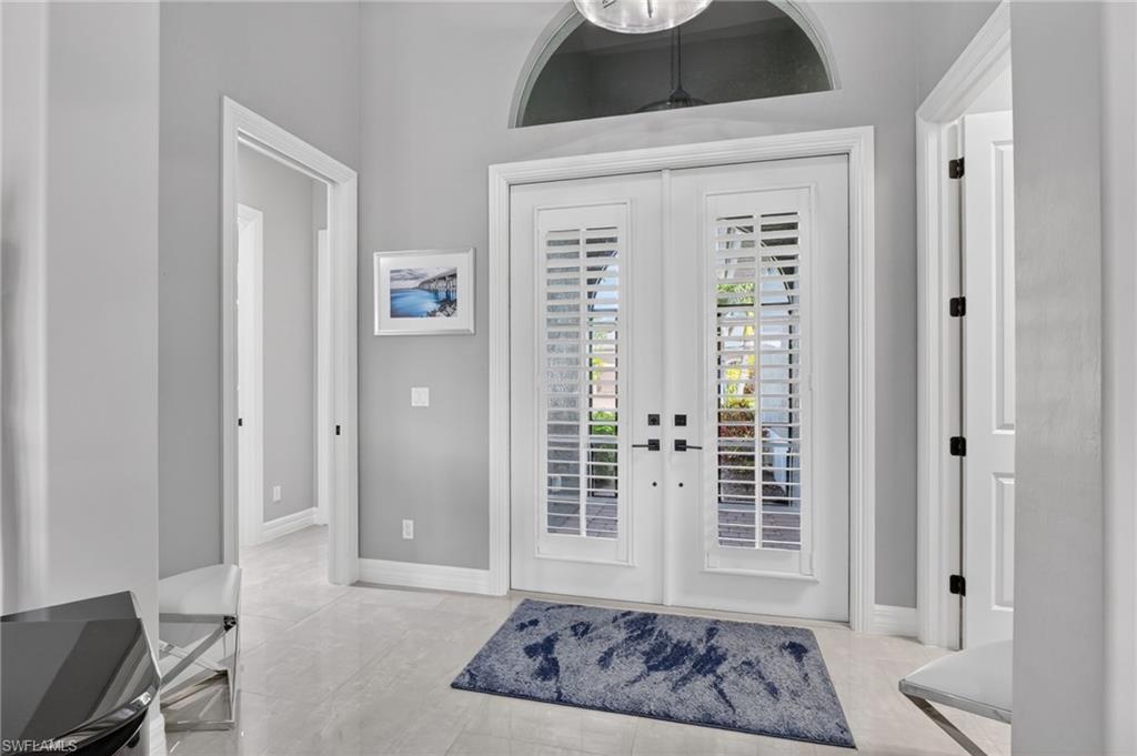 Double entry doors with interior plantation shutters, arched transom window, high ceilings, and tiled flooring