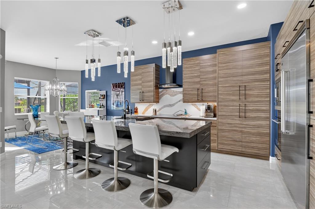 Modern kitchen featuring a large central island with wood-finish cabinetry, stainless steel appliances, a decorative backsplash, and polished tile flooring