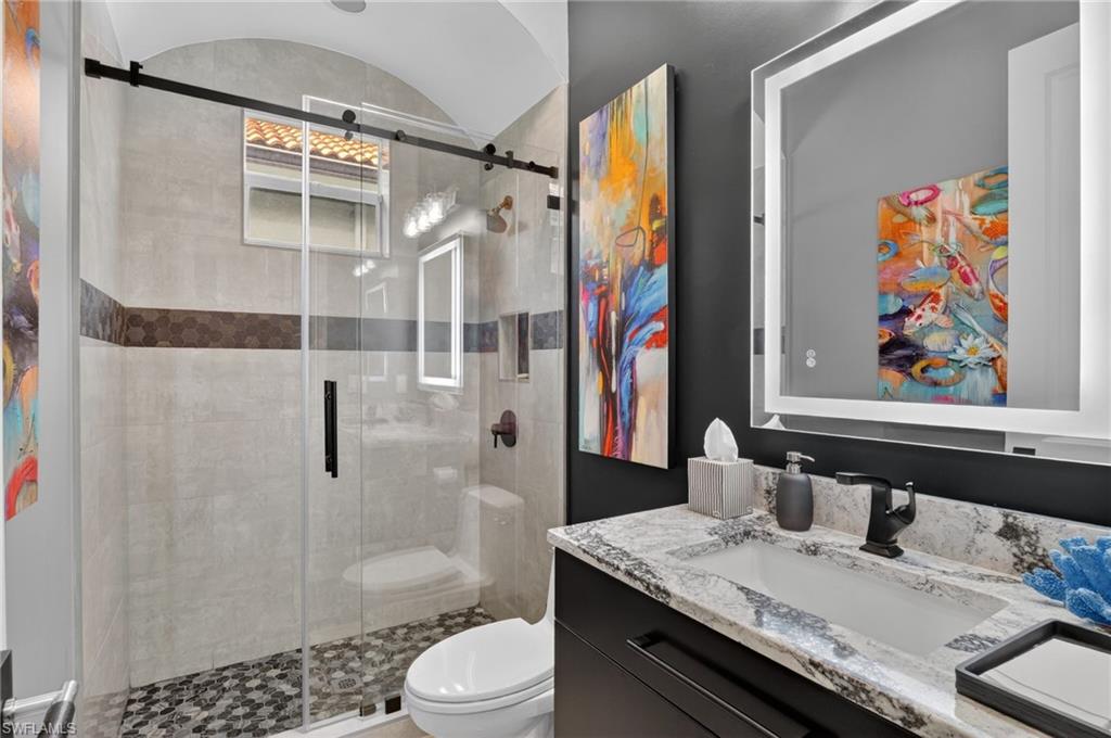 Contemporary bathroom featuring a walk-in shower with a glass sliding door, stone tile walls, and a mosaic pebble floor
