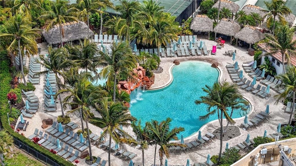 Players Club and Spa resort-style family pool area featuring a freeform swimming pool with rock waterfall, numerous lounge chairs, several thatched-roof cabanas, and mature palm trees