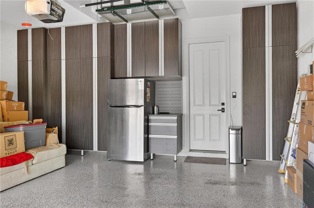 Garage featuring extensive built-in cabinetry with wood-finish doors with brushed metal accents and epoxy floor