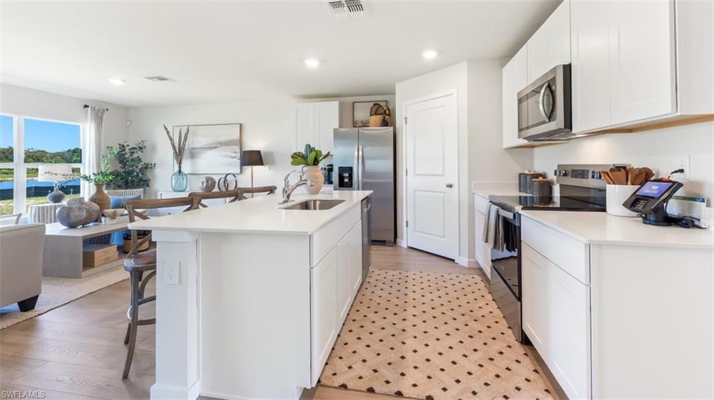 MODEL PHOTO - Kitchen featuring a kitchen breakfast bar, stainless steel appliances, white cabinets, a center island with sink, and recessed lighting