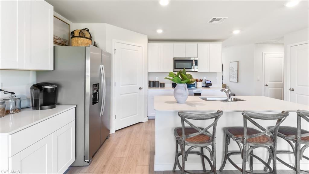 MODEL PHOTO - Kitchen with a kitchen bar, white cabinetry, appliances with stainless steel finishes, light wood finished floors, and recessed lighting