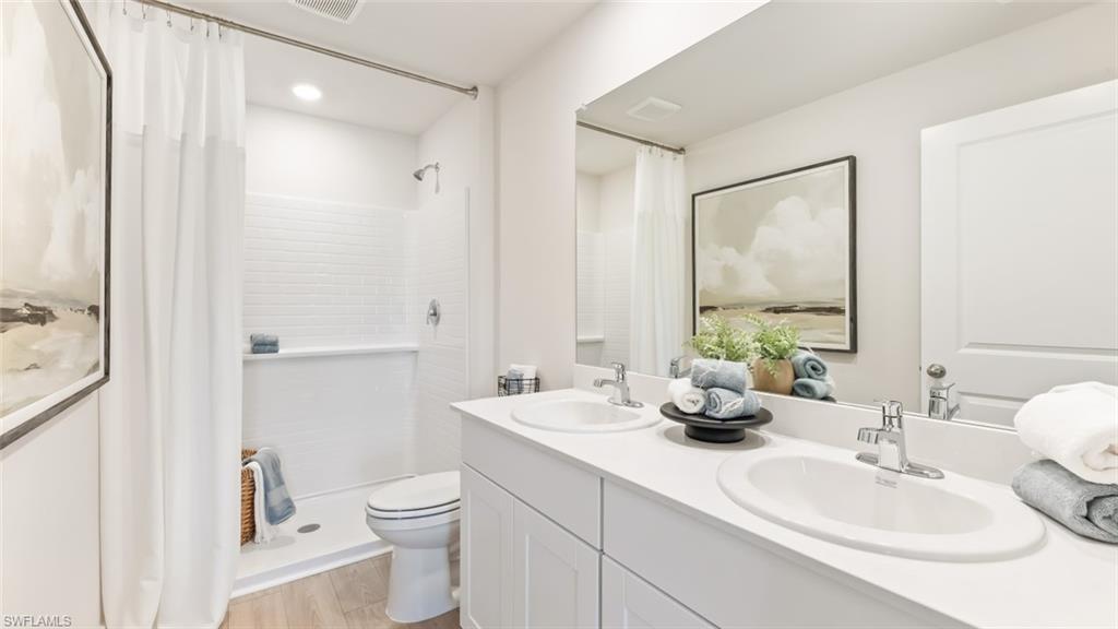 MODEL PHOTO - Full bathroom with curtained shower, double vanity, and light wood-style floors