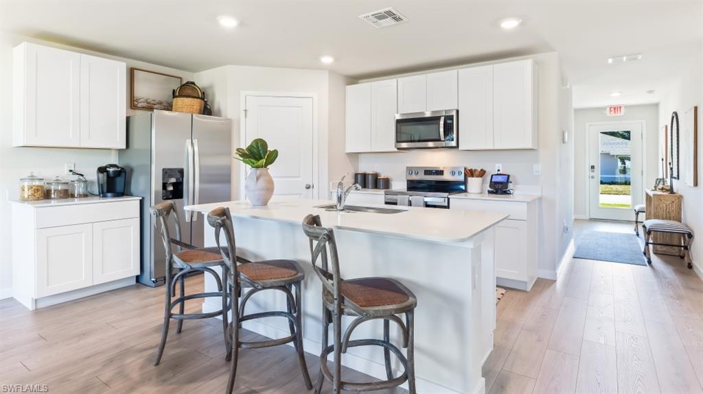MODEL PHOTO - Kitchen with appliances with stainless steel finishes, white cabinets, light wood finished floors, and recessed lighting