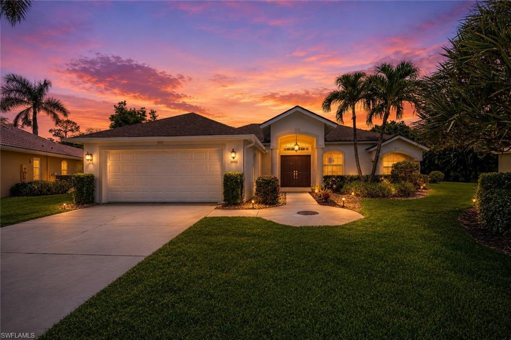 Concrete driveway and walkway with integrated lighting, attached two-car garage, manicured lawn, and mature landscaping