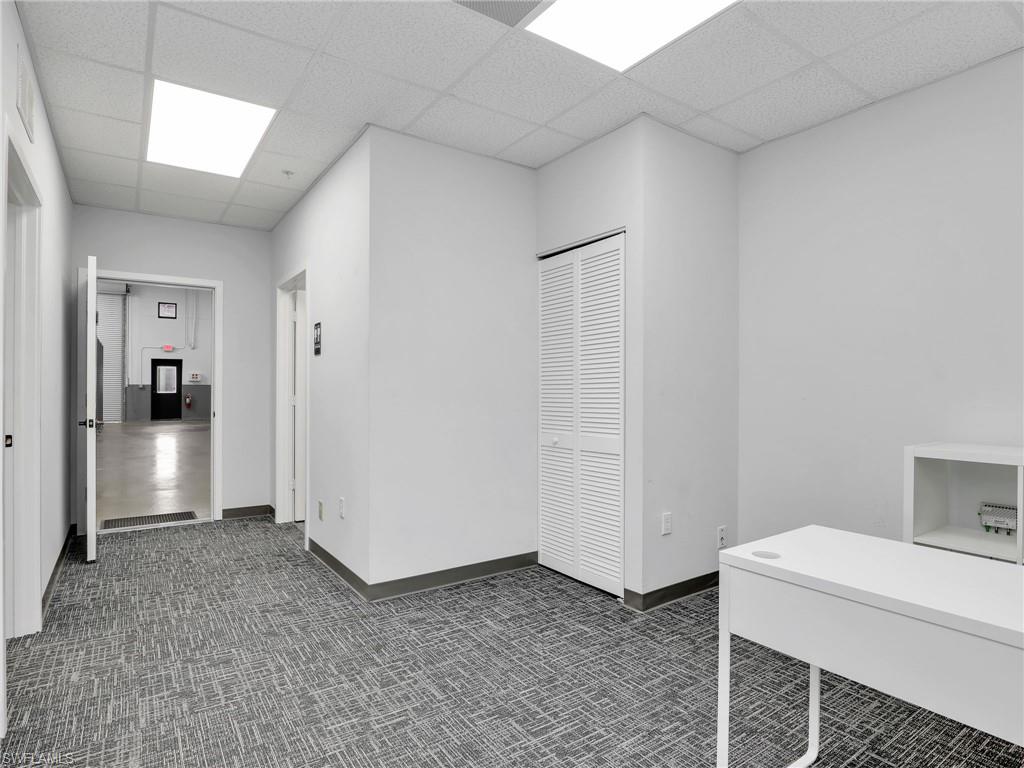 Corridor with patterned carpet flooring, drop ceiling with flush lighting, and a white louvered bifold door