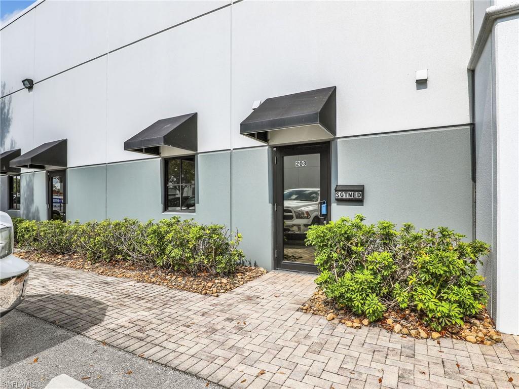 Commercial exterior featuring a block facade with a two-tone gray and white finish, multiple black awnings over windows, a glass-paneled entry door, and a paver stone walkway