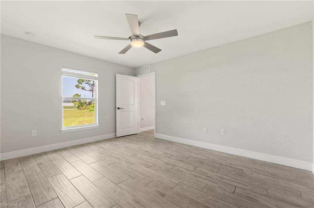 Spacious room featuring wood-finish flooring, a contemporary ceiling fan with integrated lighting, a large window providing natural illumination, a white paneled door, and neutral wall tones